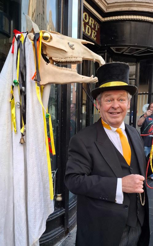 The Newport Mari Lwyd, a decorated horse's skull on a stick, held by a man under a white sheet, with her Leader in a smart suit and top hat