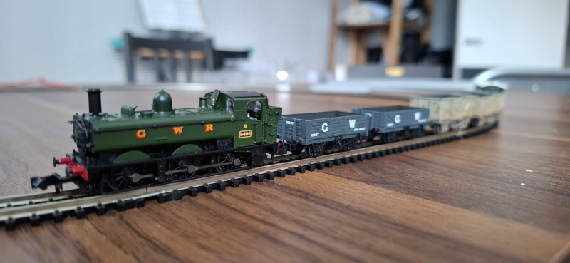 It's a train! A tiny model of a Great Western Railway steam engine, pulling some wagons, on top of a dining table